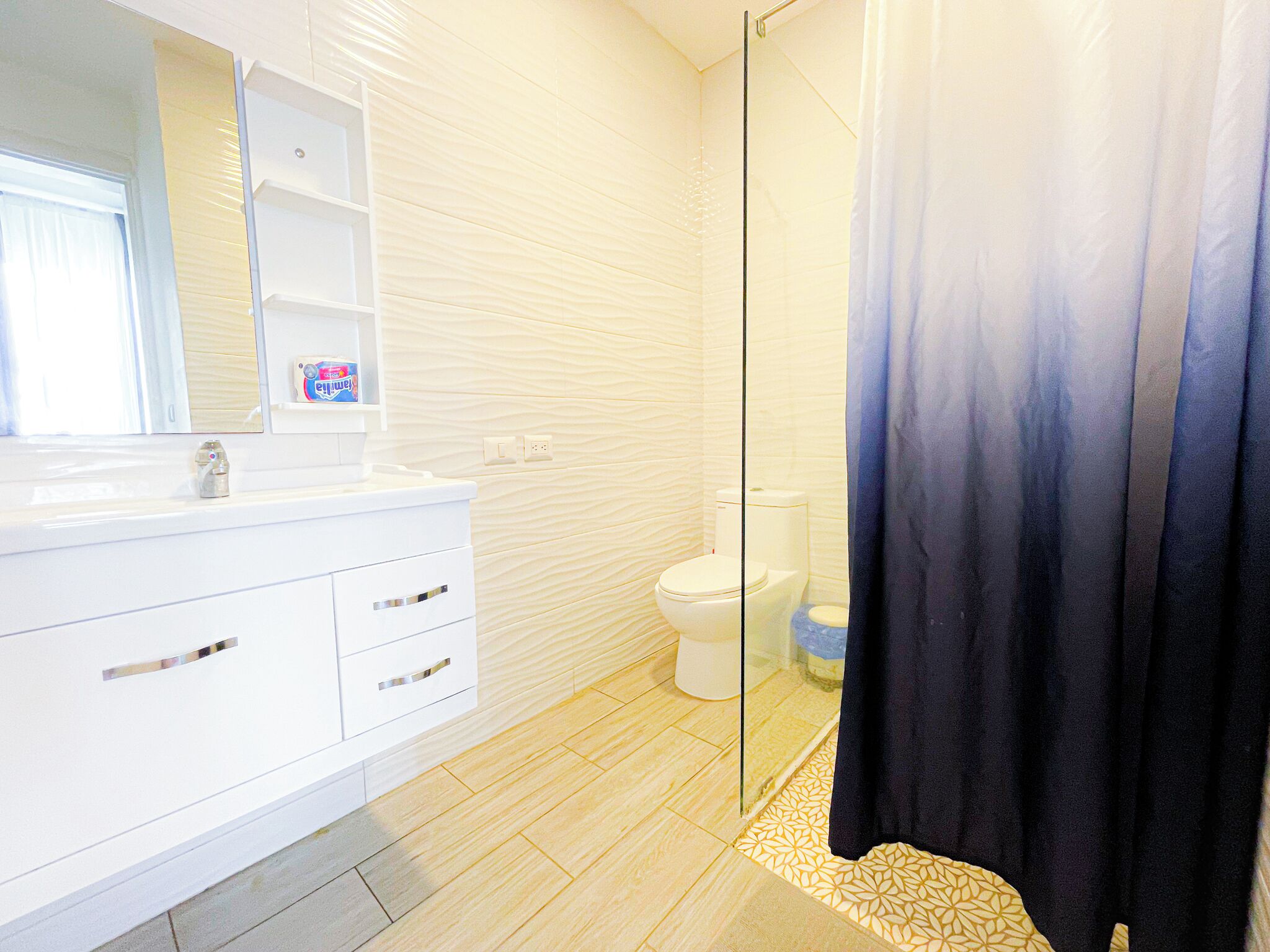 Une salle de bain moderne avec un meuble-lavabo blanc, une cabine de douche en verre et des toilettes.