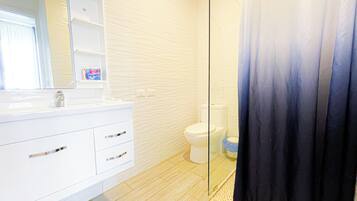Ein modernes Badezimmer mit weißem Waschtisch, einer Duschkabine aus Glas und einer Toilette.