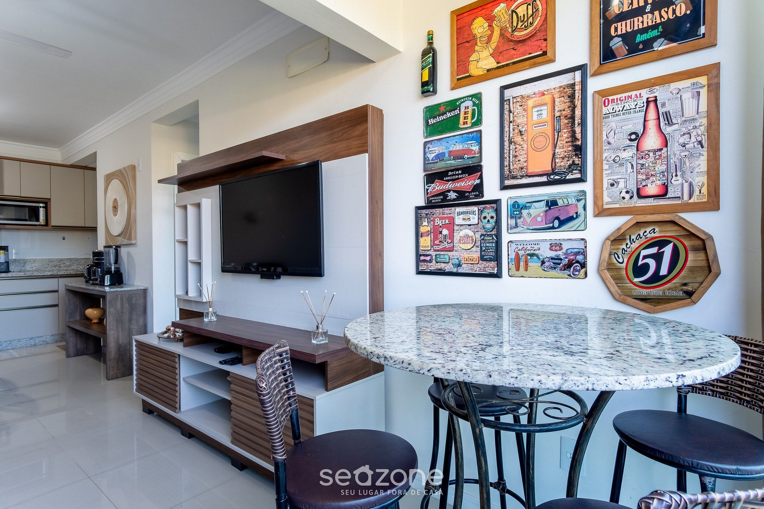 A modern living room with a flat-screen TV, a round dining table, and a wall decorated with beer-themed artwork.