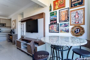 A modern living room with a flat-screen TV, a round dining table, and a wall decorated with beer-themed artwork.