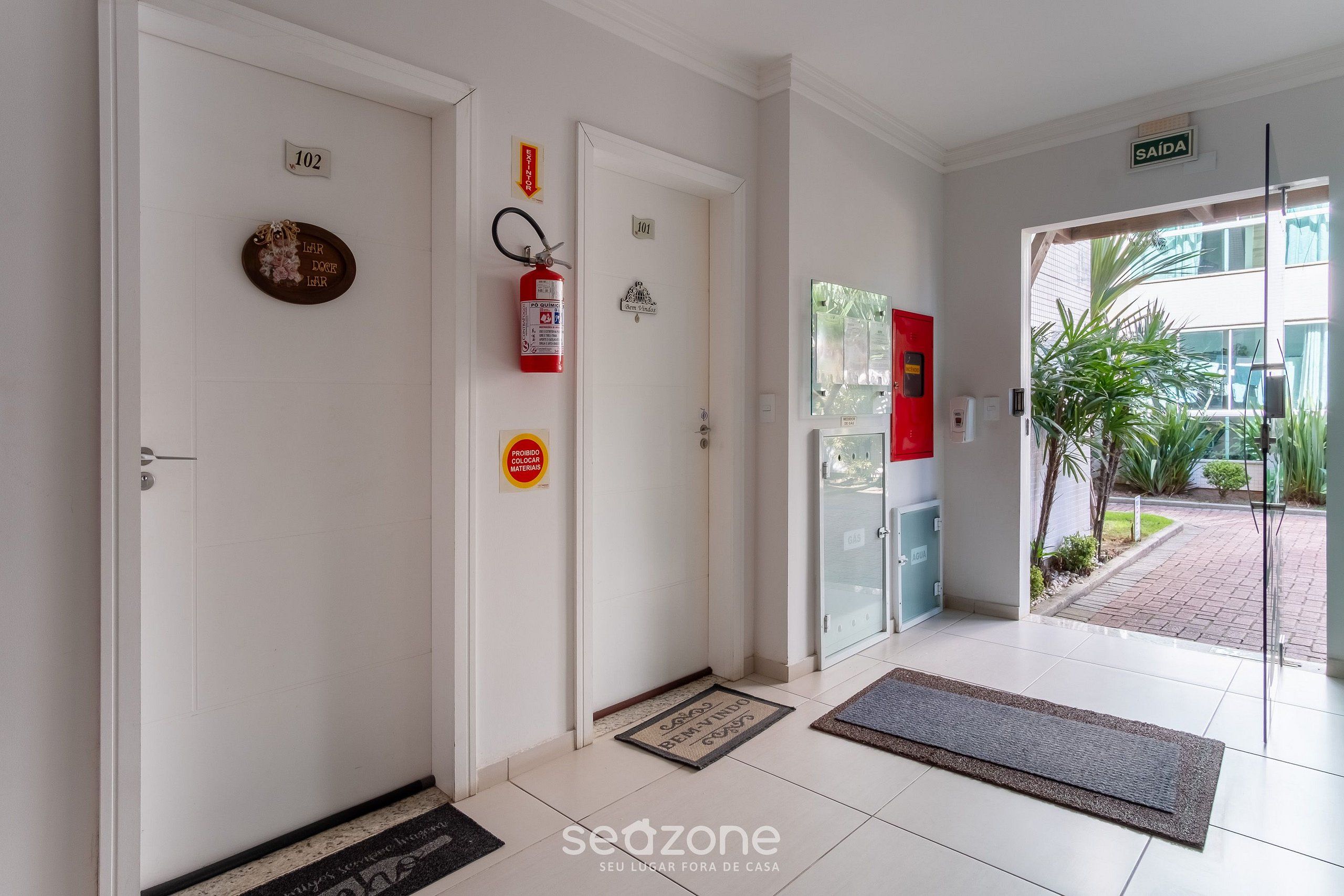 A hotel entrance with a fire extinguisher, a doormat, and a sign indicating the exit.