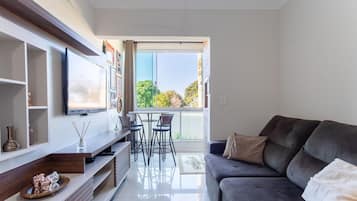 Uma sala de estar moderna com um sofá cinzento, uma televisão de tela plana e um espaço de jantar com cadeiras e uma mesa.