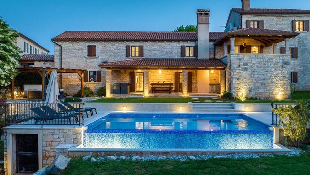 A large stone house with a swimming pool, outdoor seating, and a well-maintained lawn.