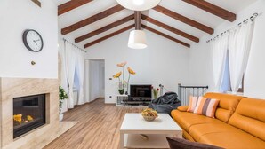 A modern living room with a fireplace, wooden beams, a sofa, a TV, and a dining table.