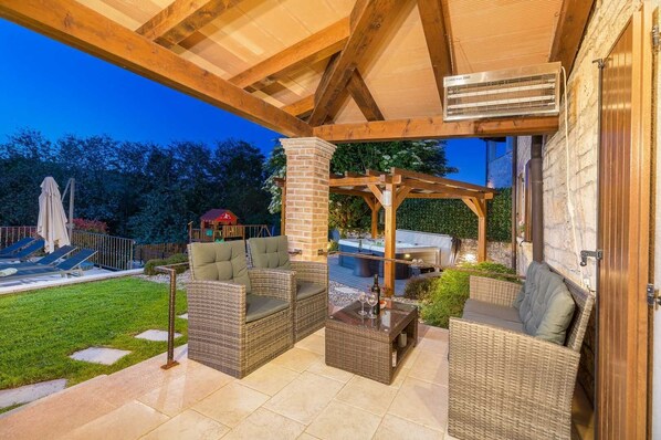 A covered outdoor patio with wicker furniture, a hot tub, and a pergola.