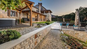 A stone house with a wooden deck, outdoor seating, and a swimming pool.