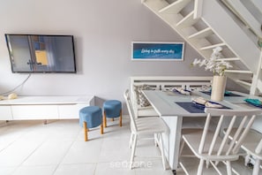 Uma zona de refeições moderna com uma mesa branca, cadeiras azuis e um banco branco. Há uma TV na parede e uma citação emoldurada acima da mesa.
