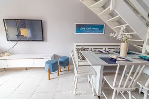 A modern dining area with a white table, blue chairs, and a white bench. There is a TV mounted on the wall and a framed quote above the table. - Duplex Overlooking Channel Cabo Frio-rj Fnx0101 (Cabo Frio)