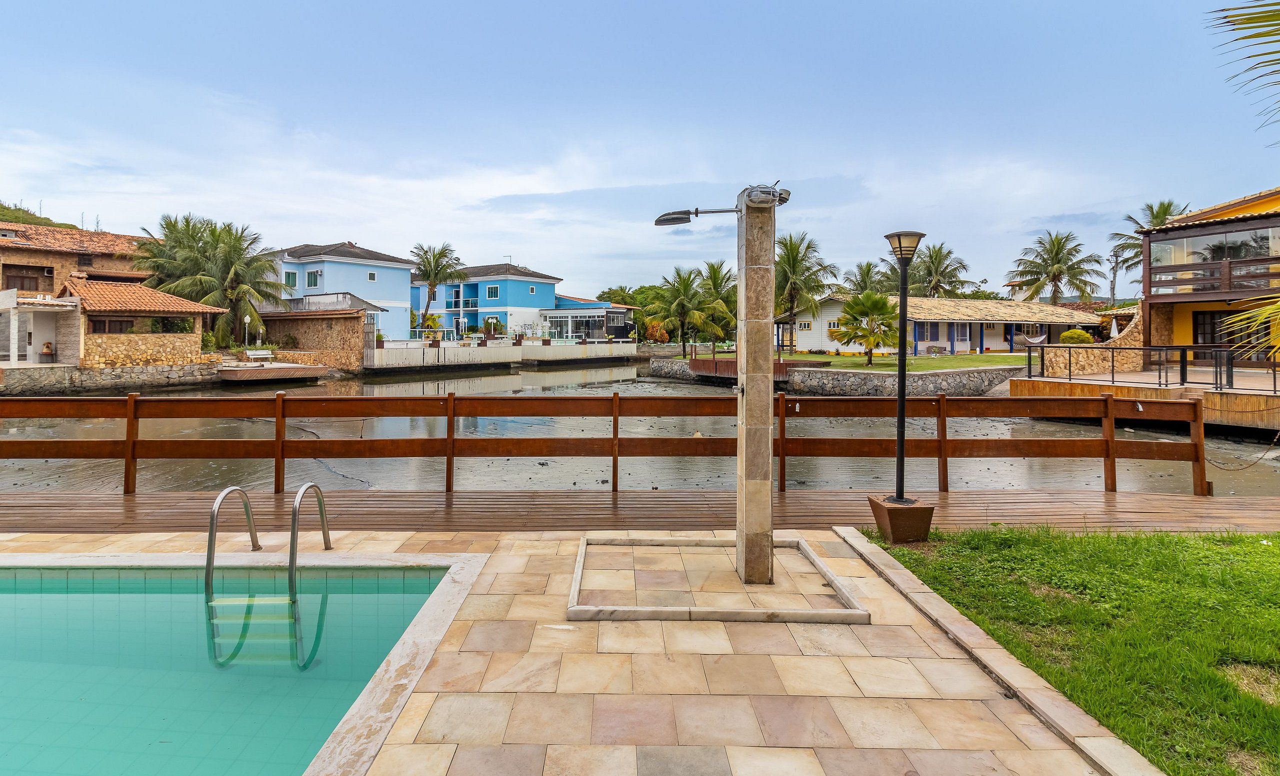 A swimming pool with a wooden deck and metal ladder, surrounded by stone walls and palm trees.