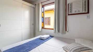 Een slaapkamer met een bed, een raam met gordijnen, een wandairconditioning en een kledingkast.