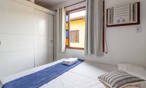 A bedroom with a bed, a window with curtains, a wall-mounted air conditioner, and a wardrobe. - Duplex Overlooking Channel Cabo Frio-rj Fnx0101 (Cabo Frio)