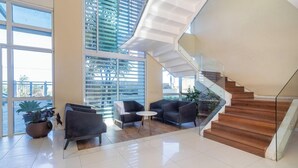 A spacious lobby with a modern staircase, large windows, and comfortable seating areas. - Apt Between Braga Beach and Forte Beach - Fmi0218 (Cabo Frio)