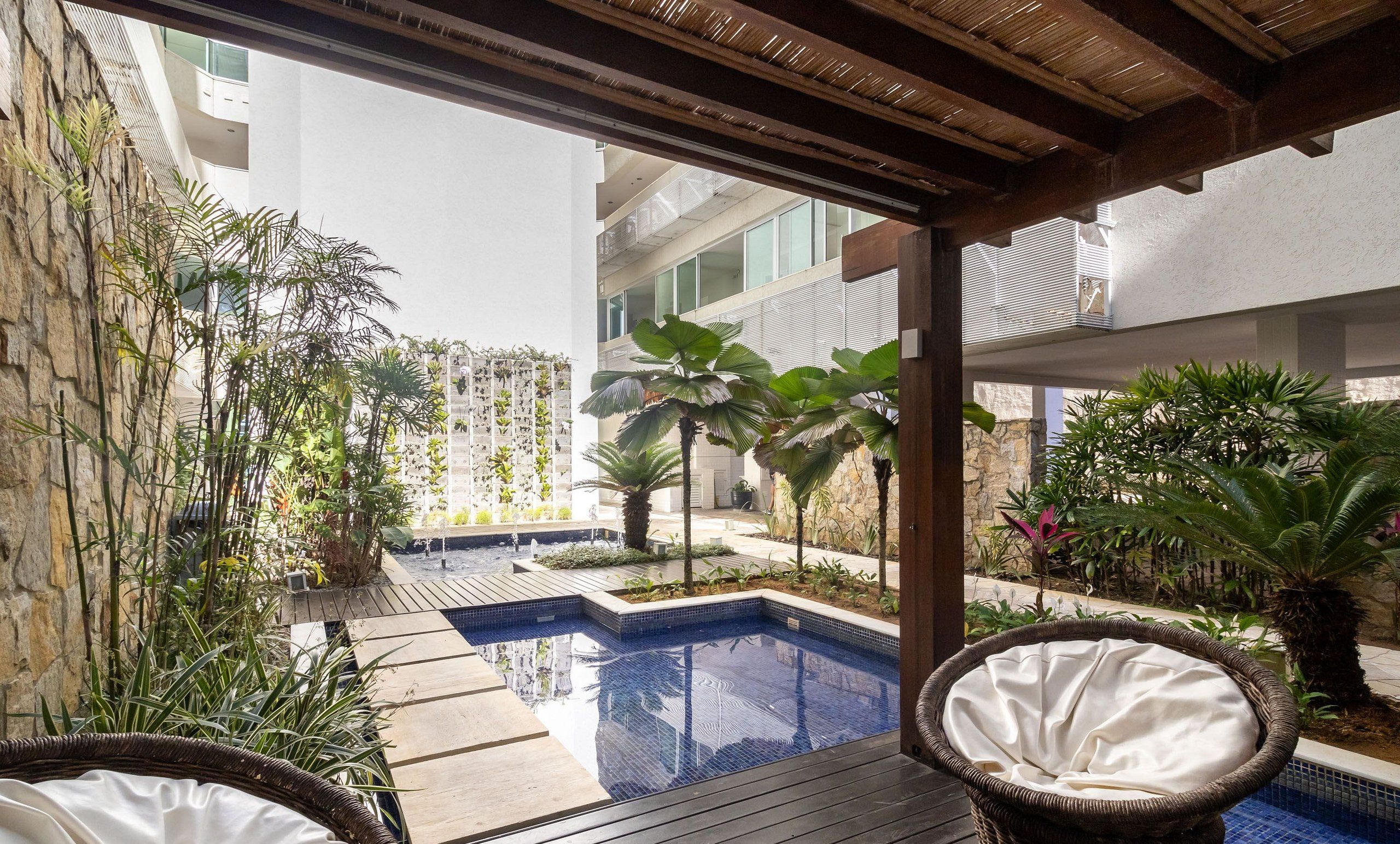 A pool area with a wooden deck, wicker chairs, and various plants.
