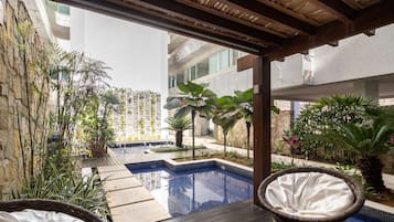 A pool area with a wooden deck, wicker chairs, and various plants.