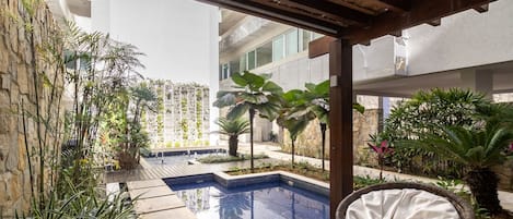 A pool area with a wooden deck, wicker chairs, and various plants.