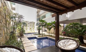 A pool area with a wooden deck, wicker chairs, and various plants. - Apt Between Braga Beach and Forte Beach - Fmi0218 (Cabo Frio)
