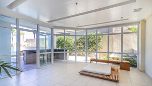 A spacious room with large windows, a wooden bench, and a bed. - Apt Between Braga Beach and Forte Beach - Fmi0218 (Cabo Frio)