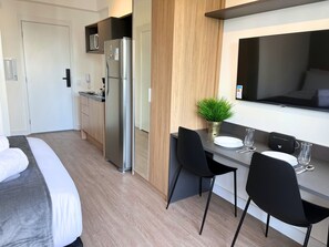 A modern hotel room with a bed, a kitchenette, a dining area with a table and chairs, and a TV mounted on the wall. - Nik Paulista (São Paulo)