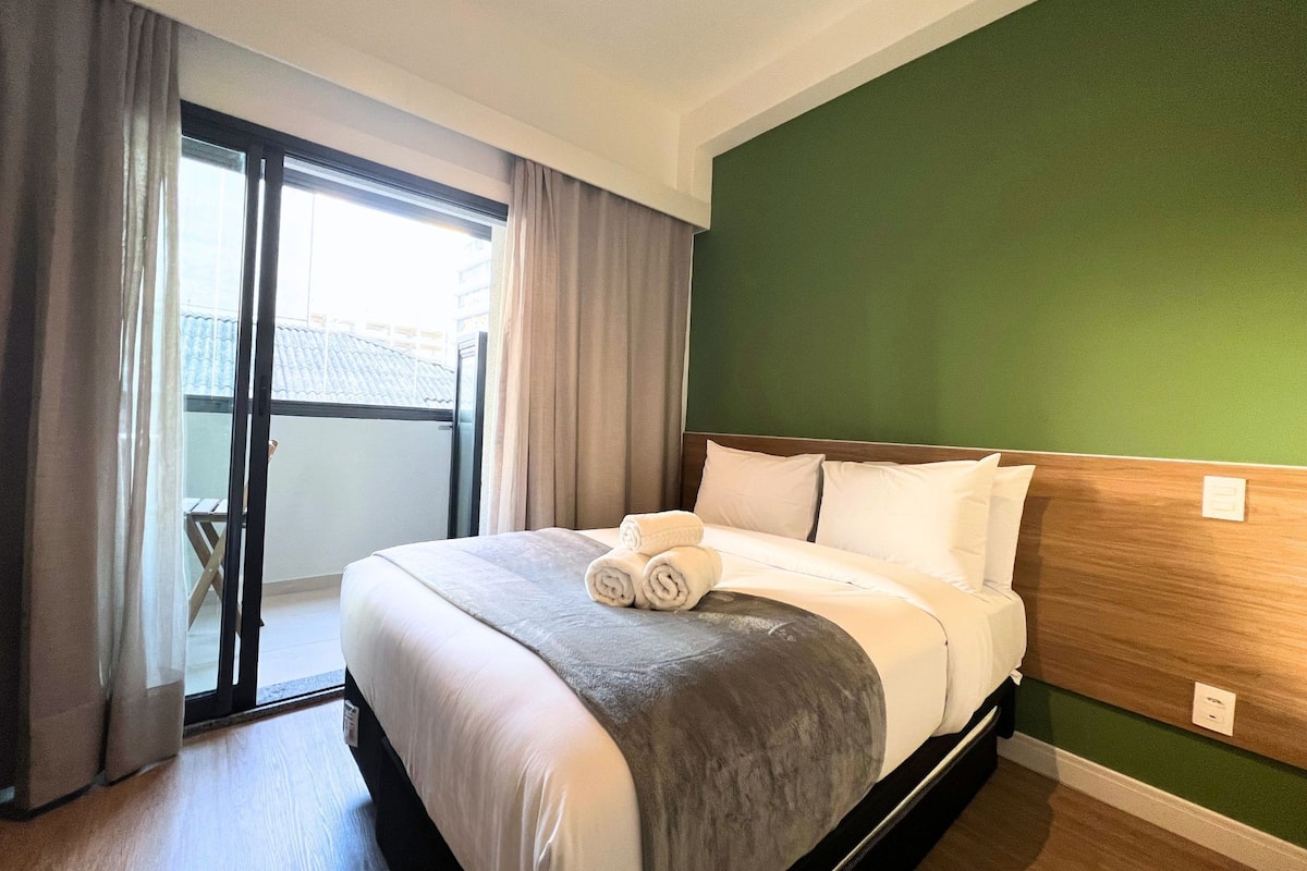 A hotel room with a bed, a green wall, and a sliding glass door to the outside.