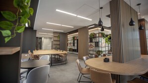 Un espacio de oficina moderno con una gran mesa de reuniones, varias mesas más pequeñas y sillas. Hay plantas y estanterías con libros y objetos decorativos.