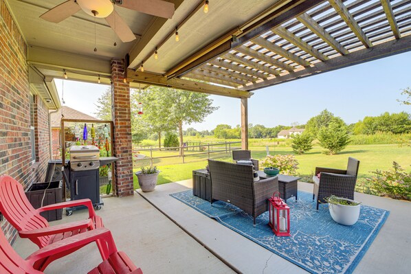Un patio techado con mobiliario exterior, una parrilla y vistas a un jardín con césped.