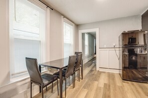 Et moderne køkken med køleskab, spisebord med stole og store vinduer med persienner.