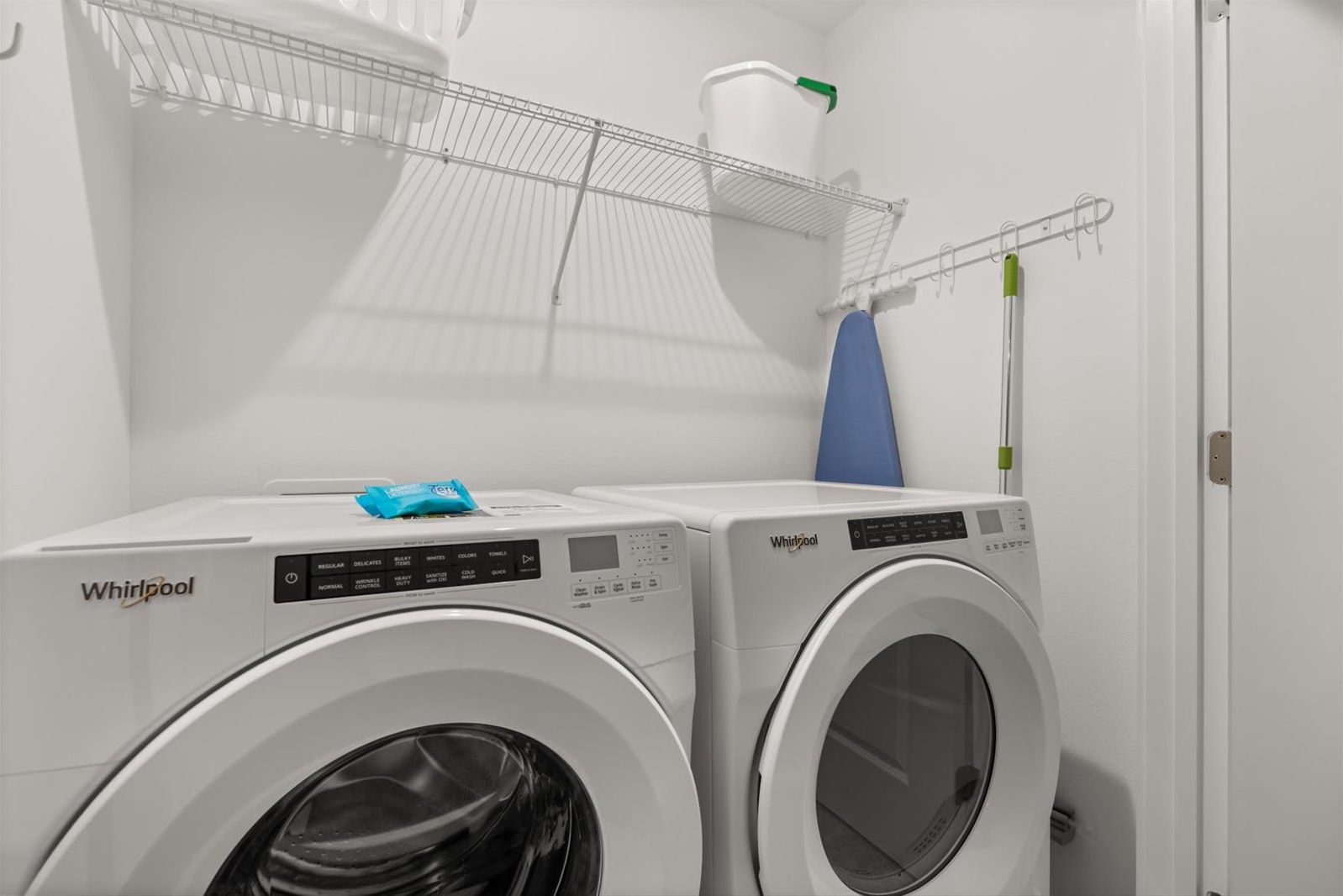 A laundry area with two Whirlpool washing machines, a metal drying rack, and a blue towel on one machine.