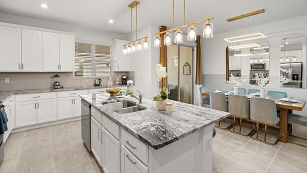 Une cuisine moderne avec des meubles blancs, un îlot en marbre et des luminaires suspendus.