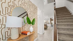 Un intérieur moderne avec un escalier, une console agrémentée d’un miroir, des livres et des plantes décoratives.