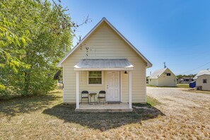 A small, single-story building with a gabled roof, a front door, and two chairs outside.
