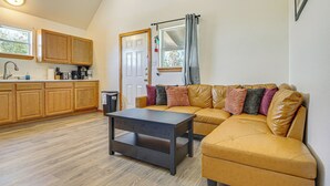 Un espacio habitable compacto con kitchenette, un sofá con cojines y una mesita.