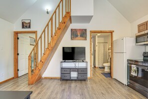 A modern kitchen with a built-in oven and microwave, a wooden staircase, and a flat-screen TV mounted on a cabinet.