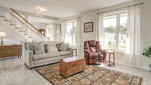 Un salon spacieux avec un escalier, un fauteuil en cuir, une table basse en bois et un tapis à motifs.