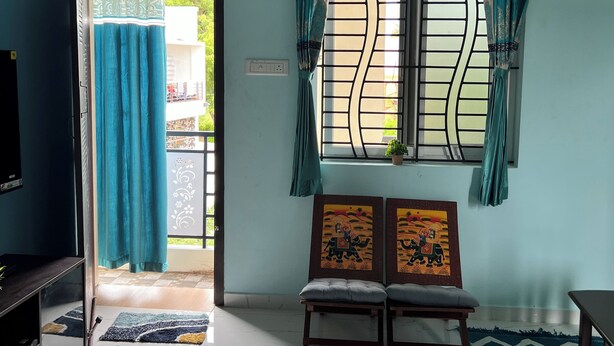 A room with a blue wall, a TV, a bench, a window with curtains, and a door leading outside.