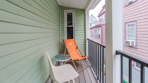 A balcony with a green exterior wall, a white chair, and an orange chair. - Cozy 4BR Home by Tufts w/ Subway Access to Downtown, MIT, Harvard + Free Parking (Medford)