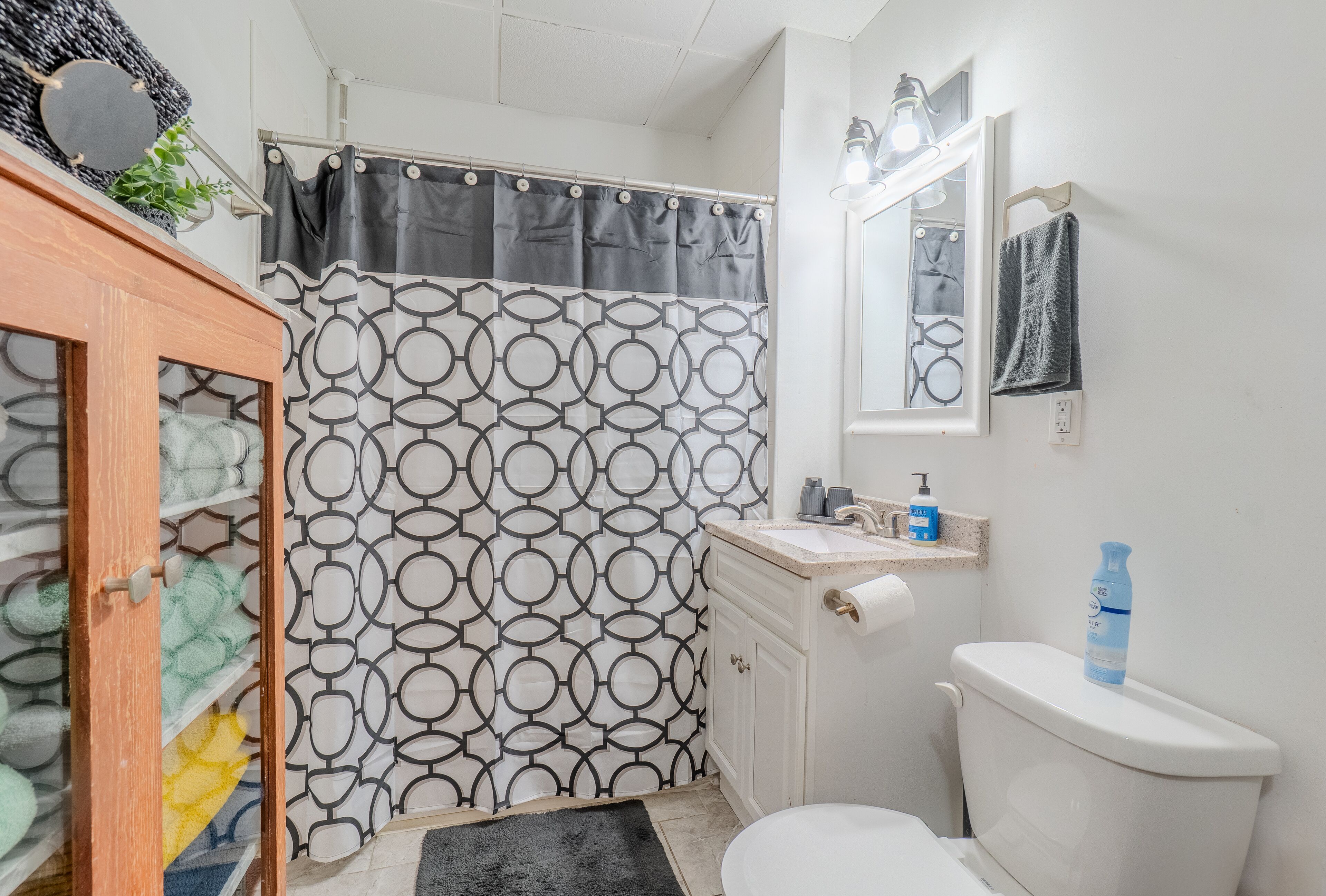 Een badkamer met een gordijn met een patroon, een toilet, een wastafel met een spiegel en een handdoekhouder.