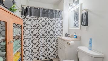 Een badkamer met een gordijn met een patroon, een toilet, een wastafel met een spiegel en een handdoekhouder.