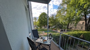 Un balcon avec une table et des chaises, une vue sur un parc et un bâtiment en arrière-plan.