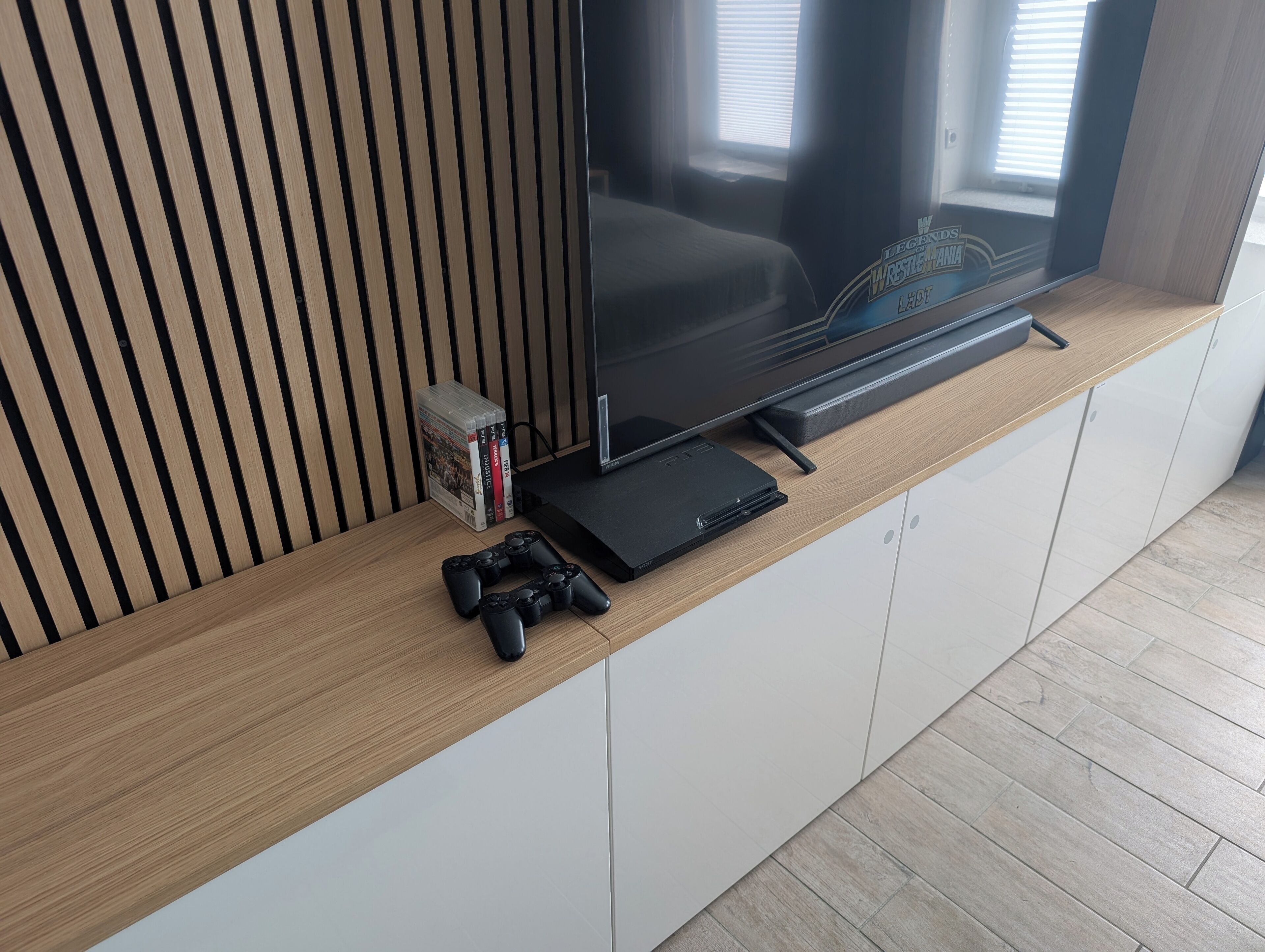A modern entertainment setup with a flat-screen TV, a gaming console, and video games on a wooden shelf.