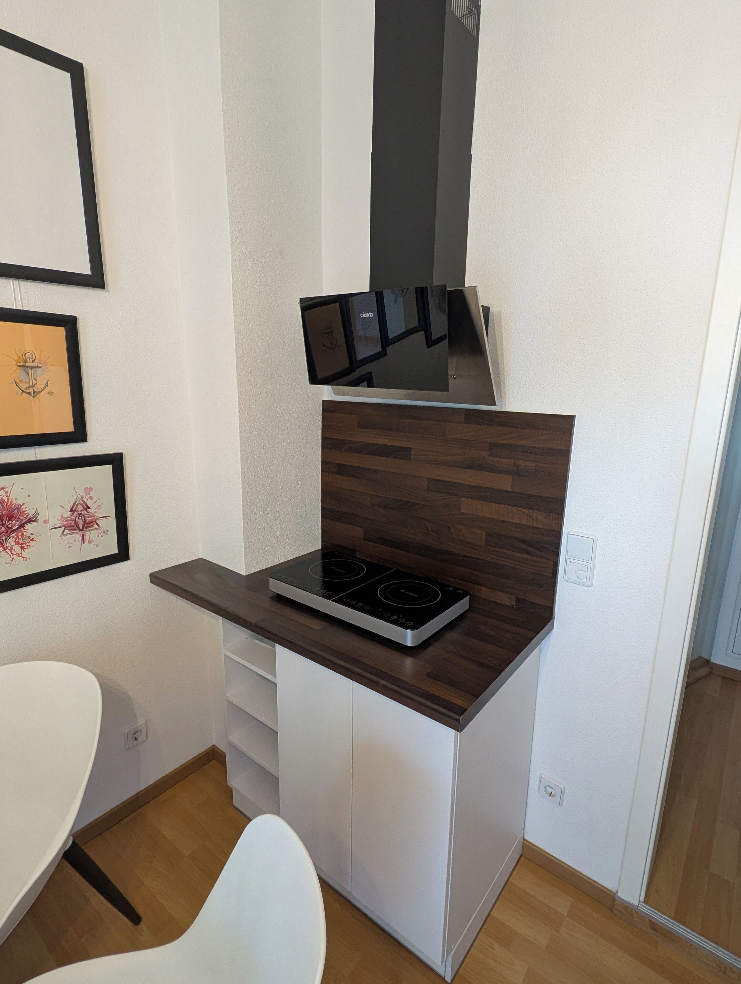 Une cuisine compacte dotée d’une cuisinière intégrée, d’un plan de travail en bois, de meubles blancs et d’œuvres d’art encadrées accrochées au mur.