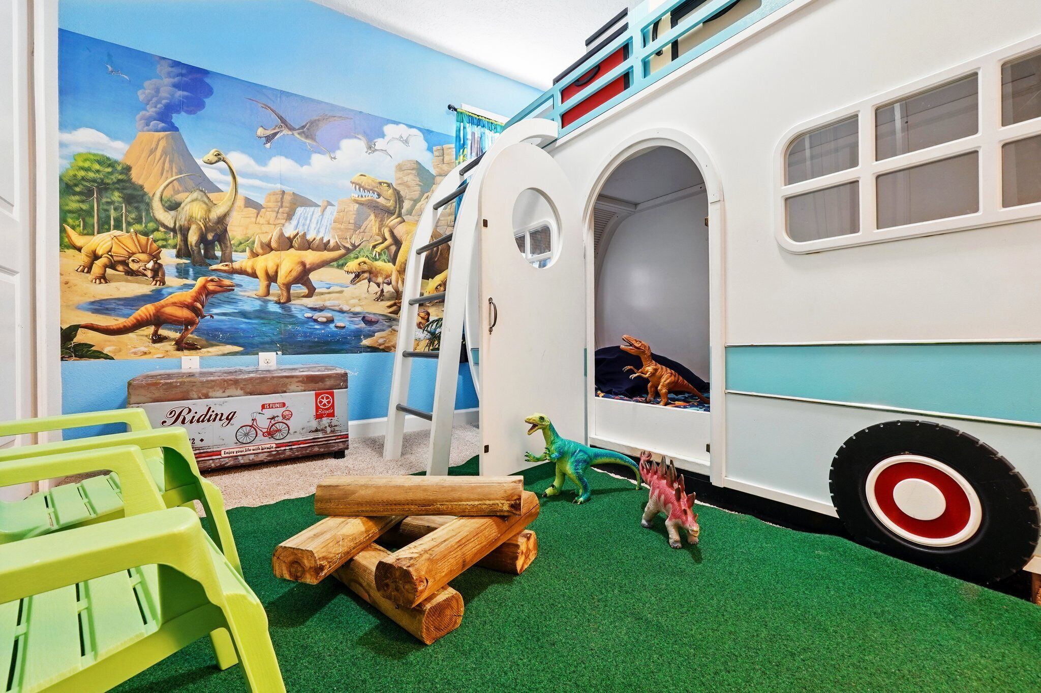 A play area with a dinosaur mural, a toy bus, and a green play table.