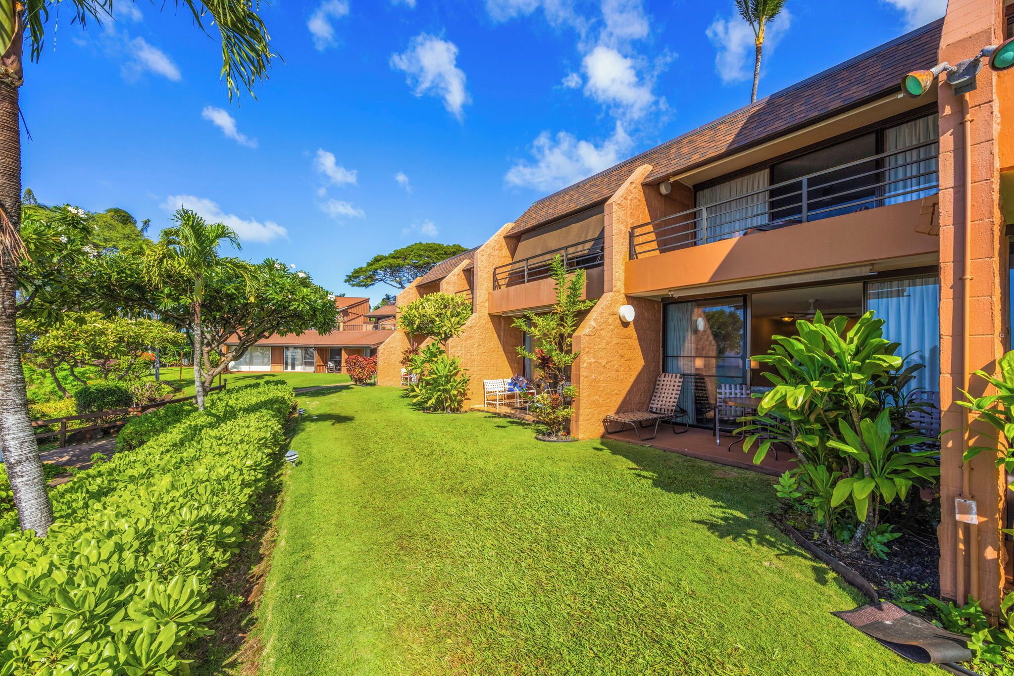 A modern hotel with a well-maintained lawn, outdoor seating, and a clear blue sky.