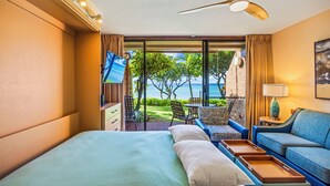 A hotel room with a bed, a sofa, a TV, and a balcony with a view of the sea. - Kuleana Club - 404 (Lahaina)