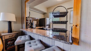 Una cocina con encimera de granito, refrigerador, microondas y pileta doble. Hay dos taburetes de bar y una cesta colgando del techo.