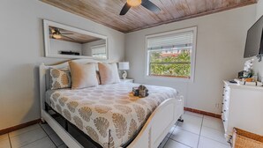 Un dormitorio con cama, mesita de noche, cómoda, ventilador de techo y ventana con persianas.