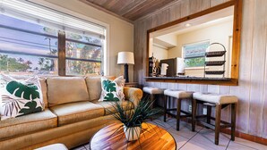 Una sala de estar con un sofá, una mesa de centro y una cocina con taburetes y mostrador.