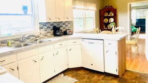 A kitchen with white cabinets, a coffee maker, and a dishwasher. There is a window with a view of the outside. - Magnolia House (Broadway)