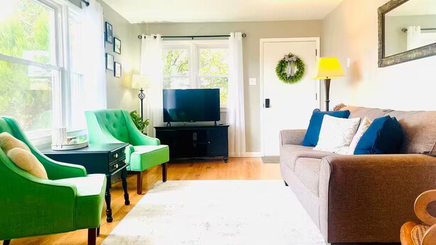 A living room with a television, green and brown sofas, a coffee table, and a large window. - Magnolia House (Broadway)