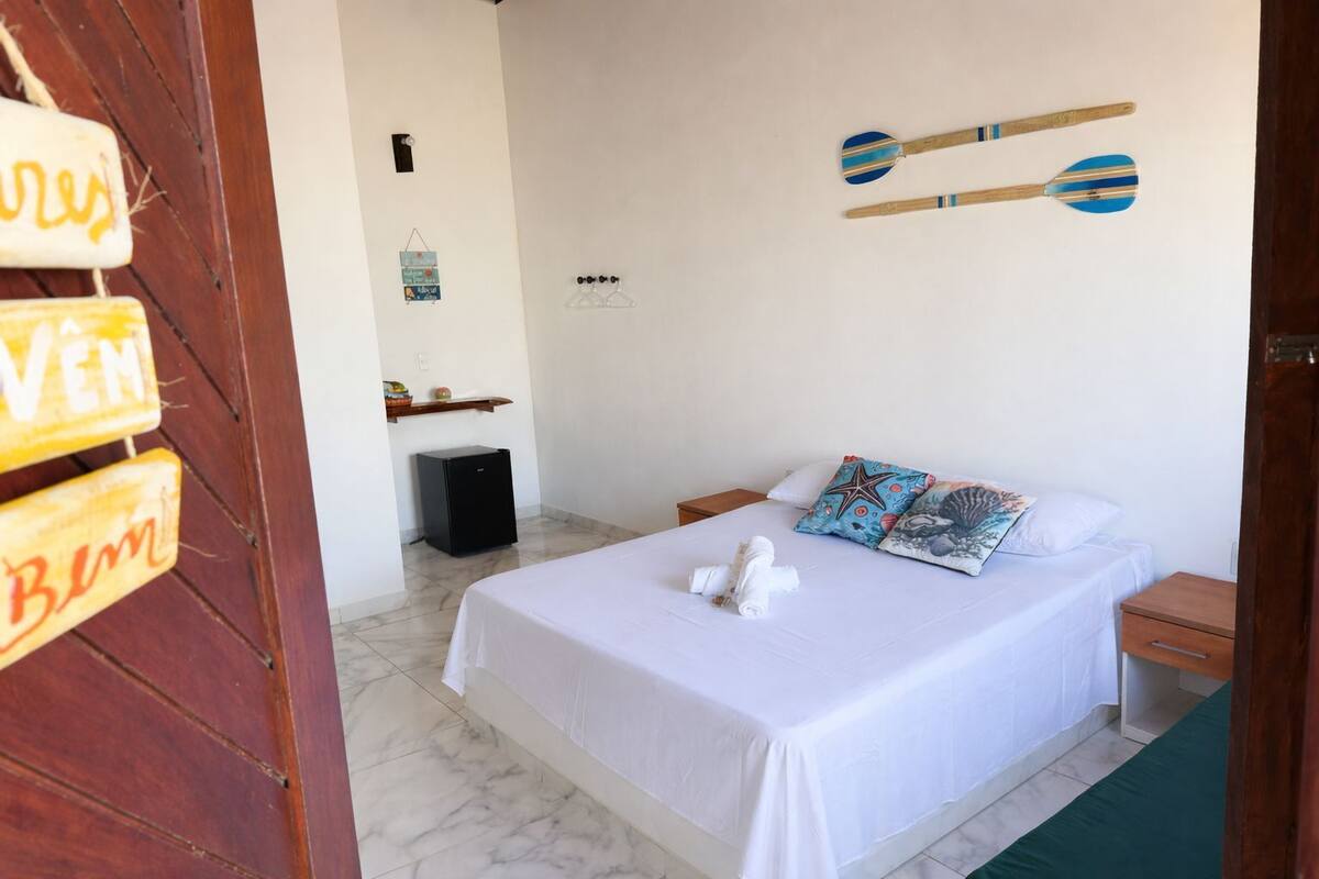 A hotel room with a bed, pillows, a small bedside table, a nightstand, a wall-mounted clock, and a door with a sign.