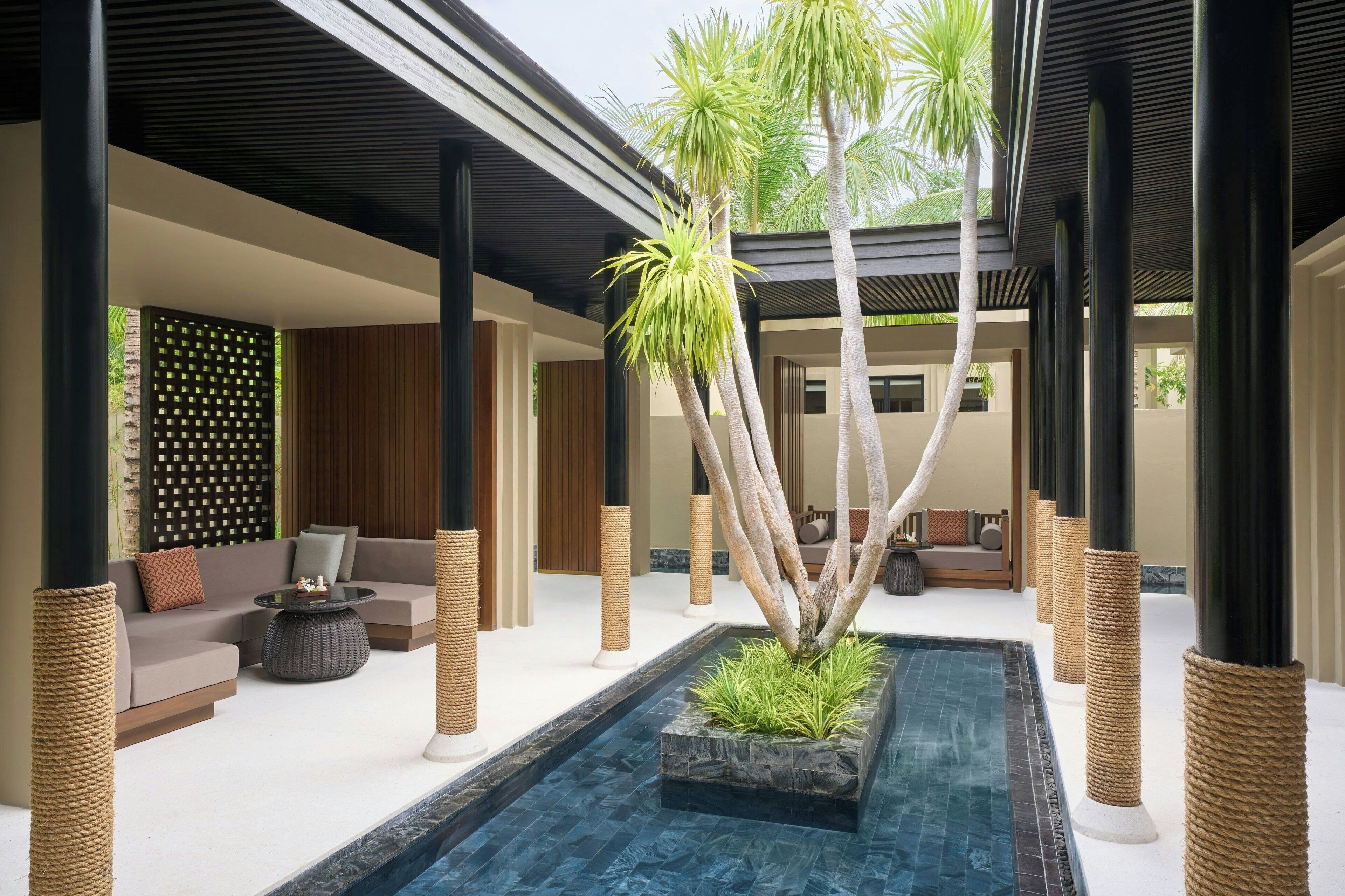 A modern indoor pool area with a central water feature, surrounded by seating and decorative plants.